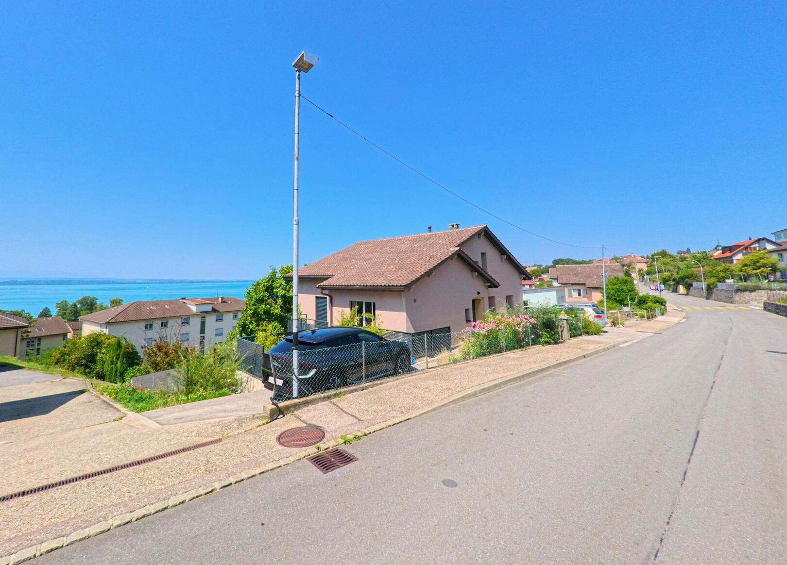 Von einer Wohnstrasse in La Grande Beroche (2023, Kanton Neuenburg) reicht der Blick ueber einzelne Einfamilienhaeuser hinweg bis zum Neuenburgersee.