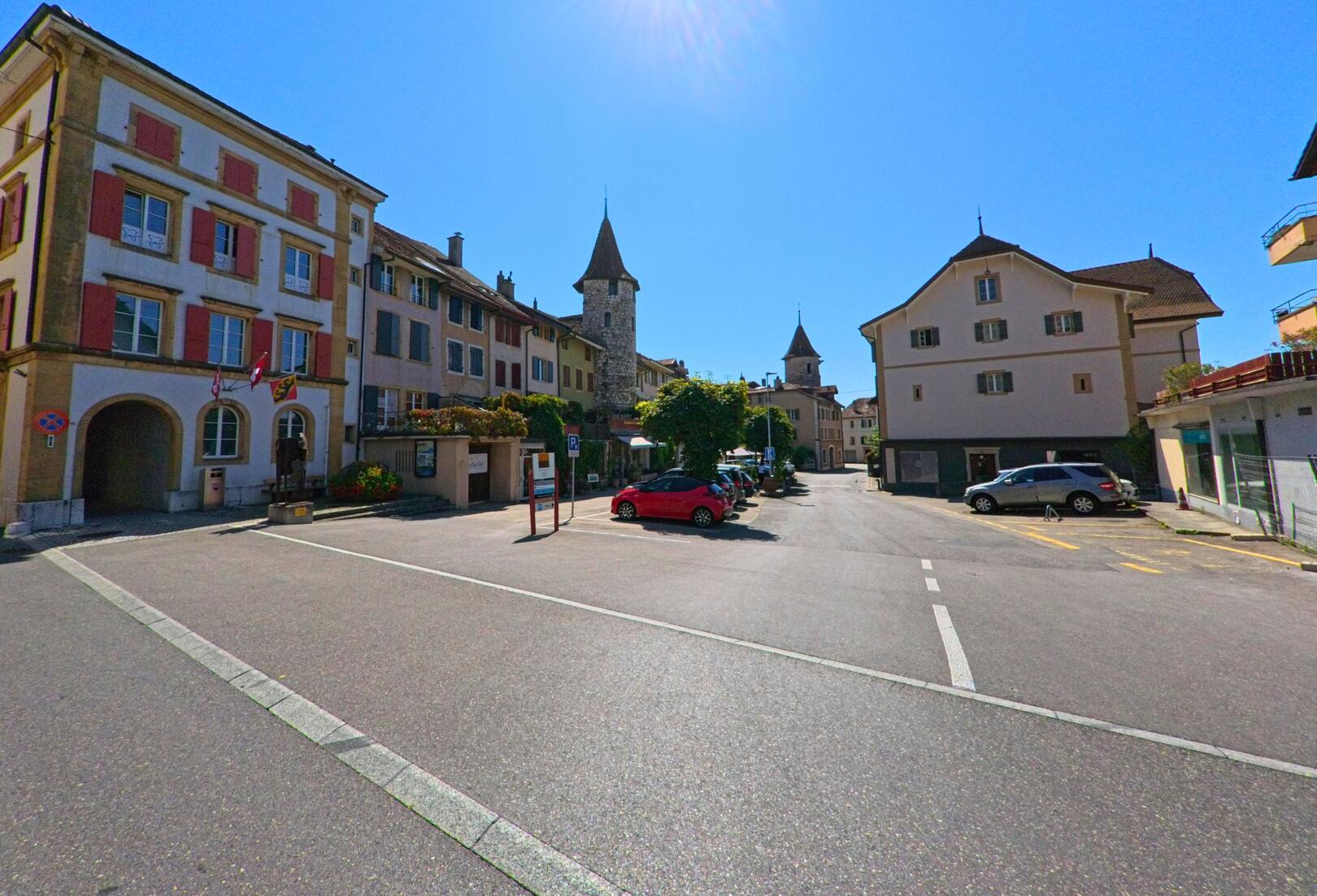 Im Zentrum von La Neuveville (2520, Kanton Bern) reihen sich historische Wohnhaeuser mit markanten Tuermen entlang einer sonnigen Strasse.