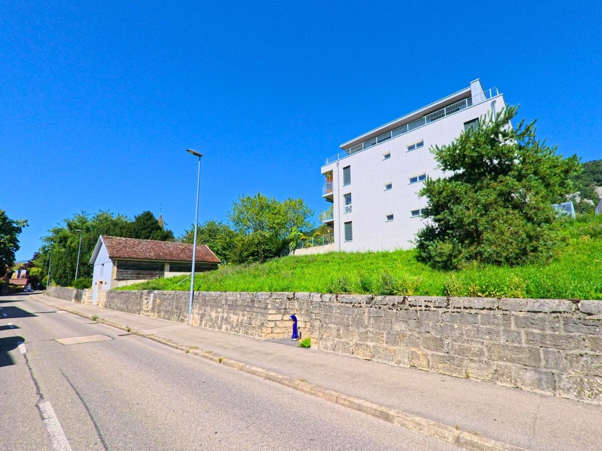 Ein modernes Wohnhaus mit Flachdach steht auf einer Gruenflaeche oberhalb einer Steinmauer in La Neuveville (2520, Kanton Bern).