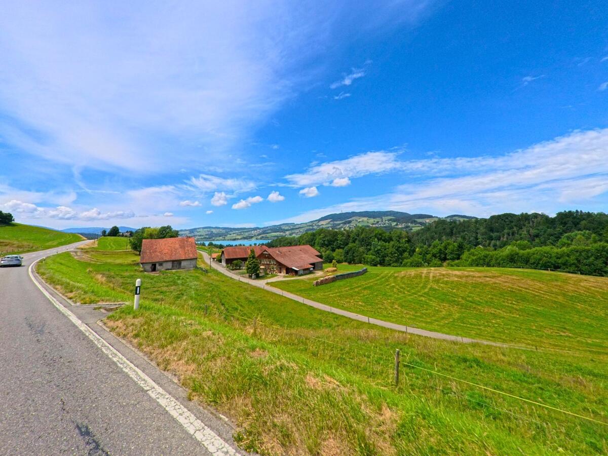 In La Roche (1634, Kanton Freiburg) liegt ein Gehöft mit mehreren Wirtschaftsgebäuden eingebettet in eine hügelige Landschaft mit weitem Ausblick.