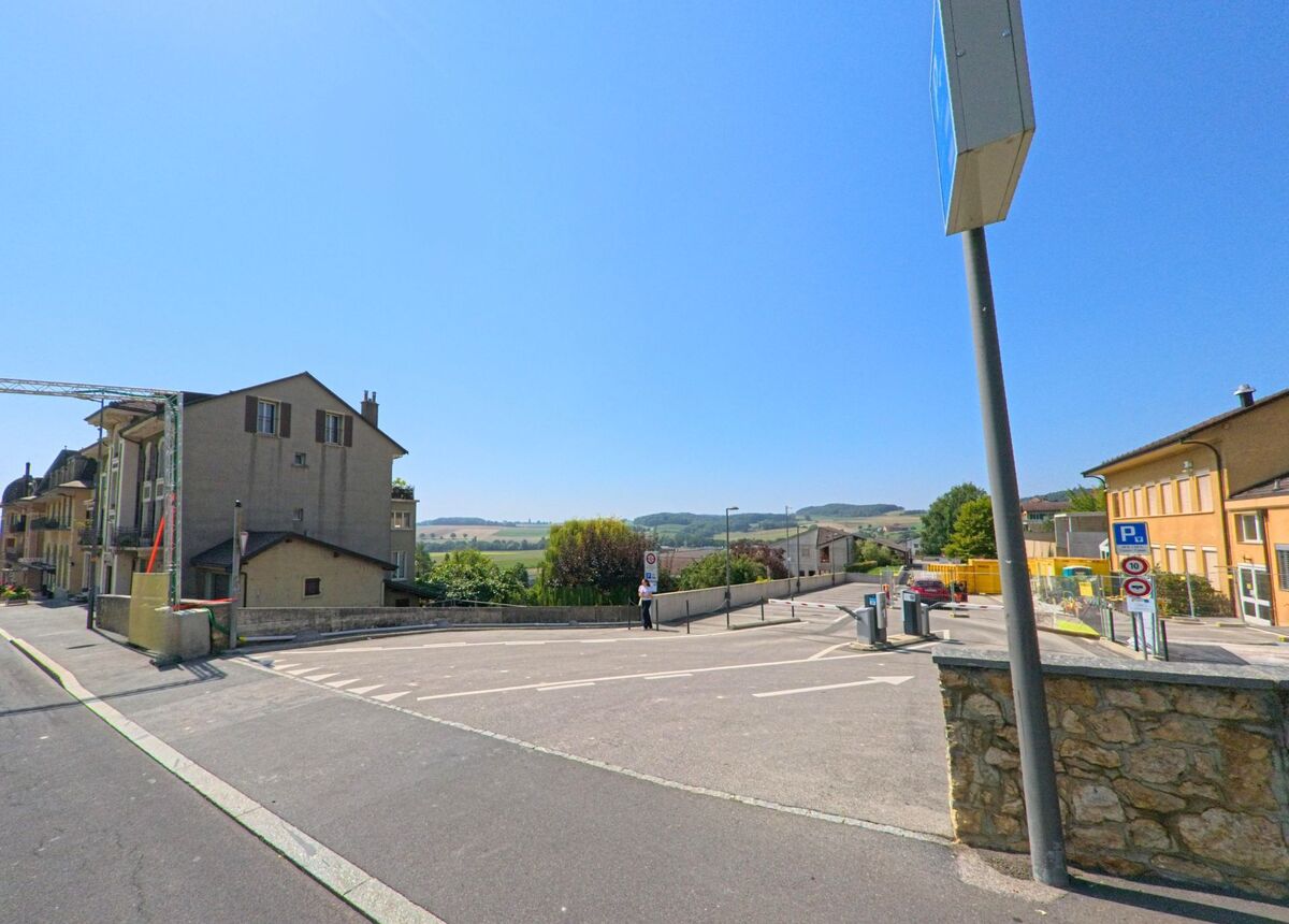 Ein Parkplatz am Ortsrand von La Sarraz (1315, Kanton Waadt) bietet freien Blick auf Haeuserzeilen und die umliegenden Huegel.