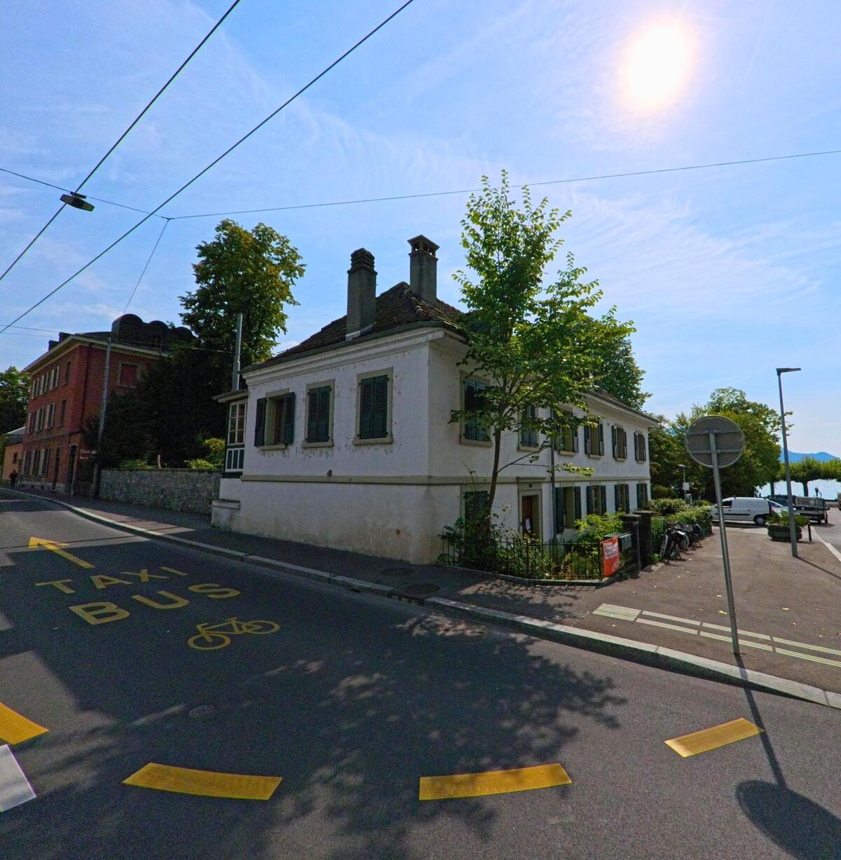 Ein altes Haus mit gruenen Fensterlaeden steht nahe dem Seeufer in La_Tour-de-Peilz (1814, Kanton Waadt) an einer Strasse mit Taxi- und Busspur.