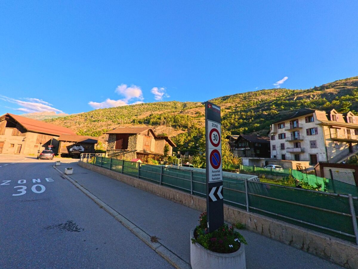 Ein Strassenschild markiert in Lalden (3931, Kanton Wallis) eine Tempo-30-Zone, umgeben von traditionellen Wohnhaeusern und Berghaengen im Abendlicht.