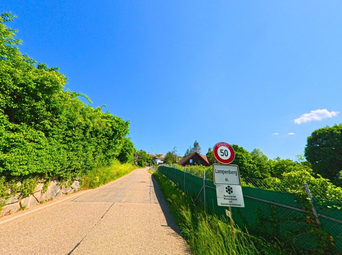 Ein Strassenschild am Ortseingang von Lampenberg (4432, Kanton Baselland) markiert die Tempobegrenzung auf einer schmalen Zufahrtsstrasse mit dichter Vegetation.