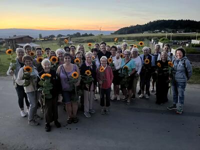 Bei Abendlicht steht eine Gruppe des Landfrauenvereins in Kerzers (3210, Kanton Freiburg) mit Sonnenblumen vor offener Landschaft zusammen.