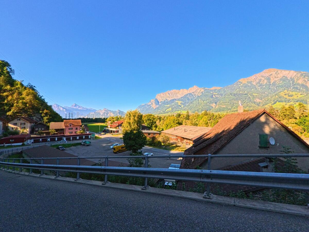 Blick über den Ortsteil von Landquart (7303, Kanton St. Gallen) mit farbigen Häusern und weitem Alpenpanorama im Hintergrund unter klarem Himmel.