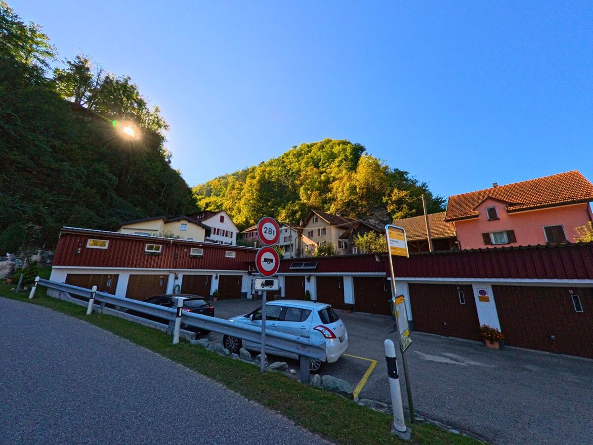 Am Waldrand von Landquart (7303, Kanton St. Gallen) stehen mehrere Wohnhäuser mit Garagen, während die Sonne durch die Bäume am Hang scheint.