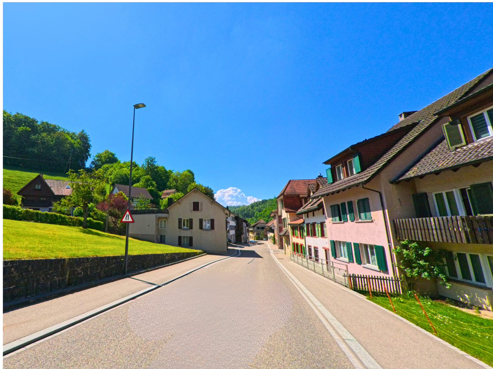Die Hauptstrasse von Langenbruck (4438, Kanton Baselland) verläuft zwischen traditionellen Wohnhäusern und einem leicht ansteigenden Wiesenhang am sonnigen Ortsrand.