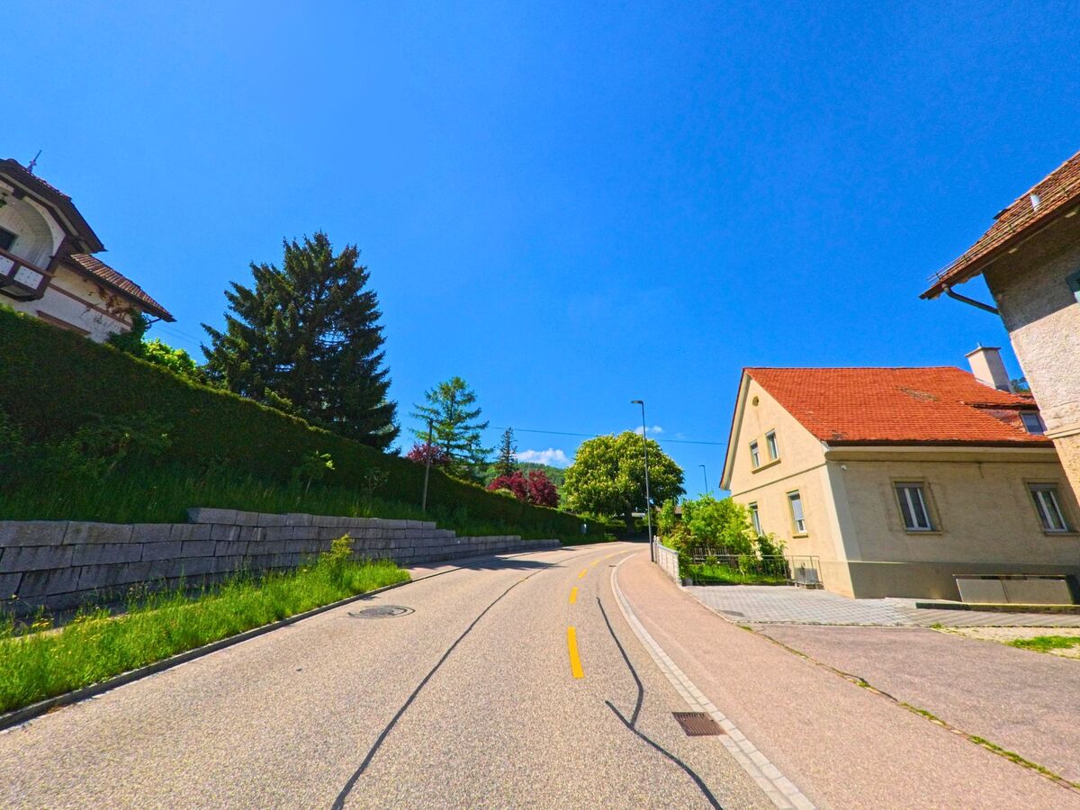 In Langenbruck (4438, Kanton Baselland) windet sich eine ruhige Quartierstrasse mit Einfamilienhäusern und Gartenmauern sanft den Hang hinauf.