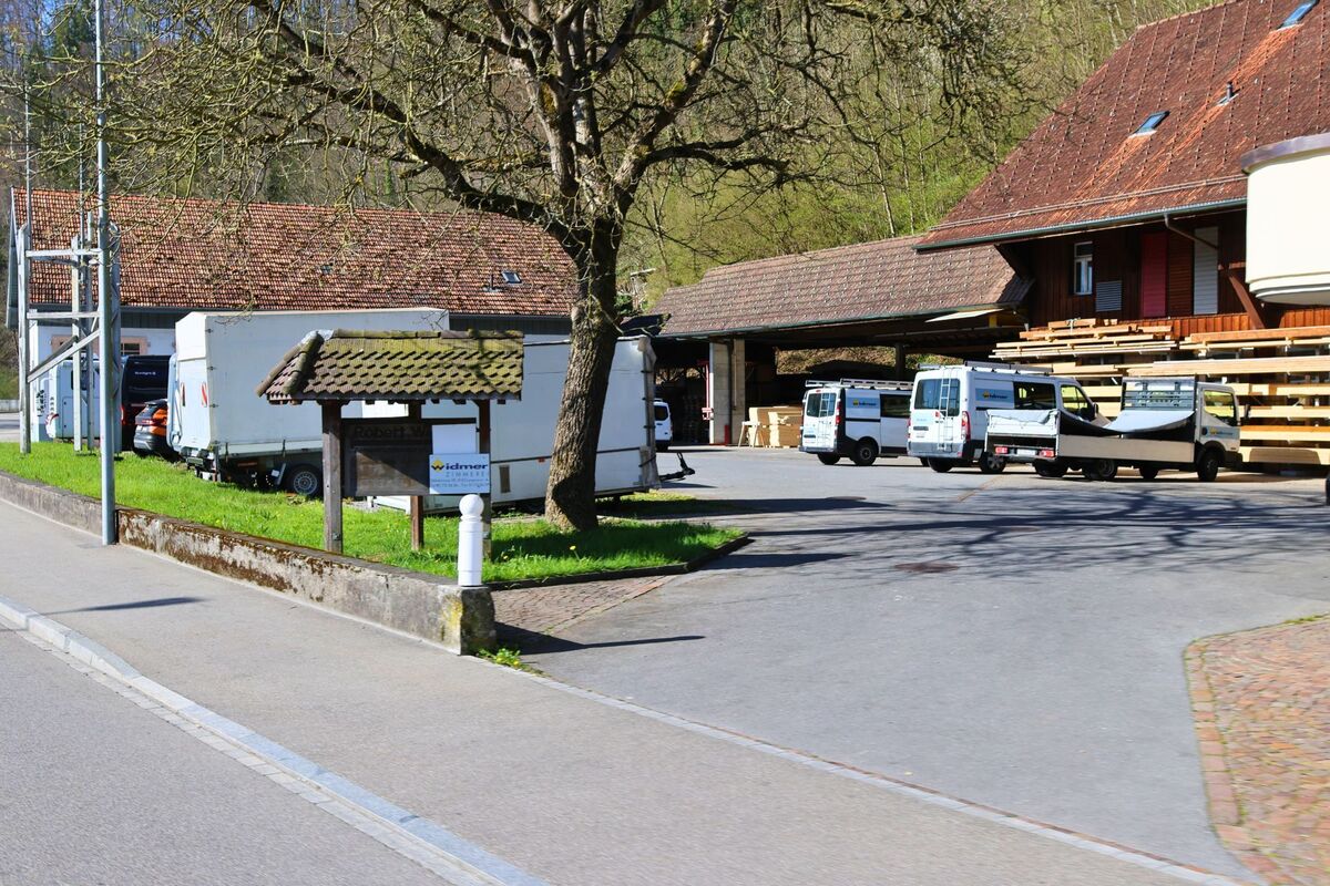 Ein Handwerksbetrieb mit mehreren Transportfahrzeugen und Holzlager befindet sich in Langnau am Albis, 8135 im Kanton Zürich, am Rand eines bewaldeten Hangs.