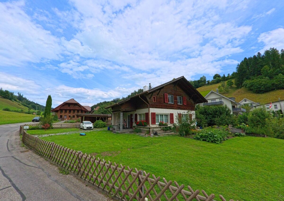 Ein traditionelles Emmentaler Haus mit roten Fensterlaeden und gepflegtem Garten steht in Langnau im Emmental (3550, Kanton Bern) am Rand eines sanft ansteigenden Huegellands.