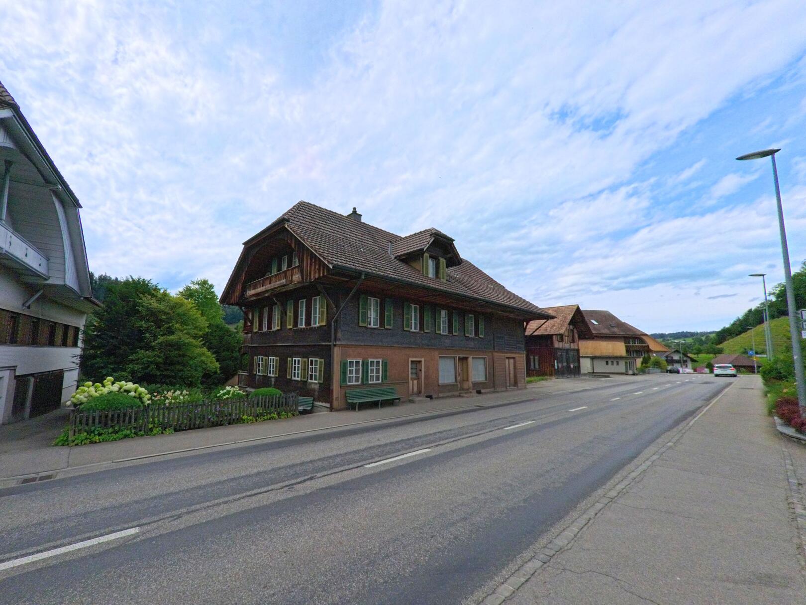 Entlang der Hauptstrasse in Langnau im Emmental (3552, Kanton Bern) stehen traditionelle Emmentaler Haeuser mit dunkler Holzfassade und gepflegtem Vorgarten.