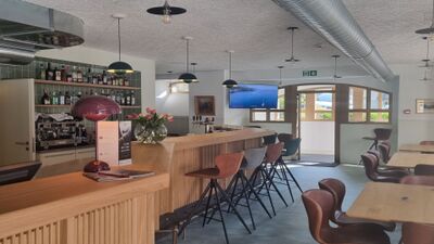 Im Inneren der L’Auberge de la Bourgeoisie in Troistorrents (1872, Kanton Wallis) lädt eine moderne Bar mit Holztischen, bequemen Stühlen und warmem Licht zu einem gemütlichen Aufenthalt ein.