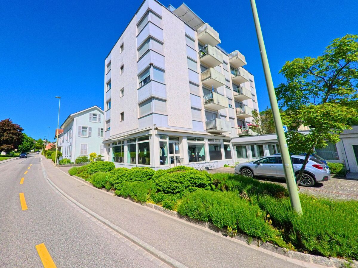 Entlang einer Hauptstrasse in Laufen (4242, Kanton Baselland) reihen sich moderne und traditionelle Wohngebaeude mit gepflegter Vorgartenzone.