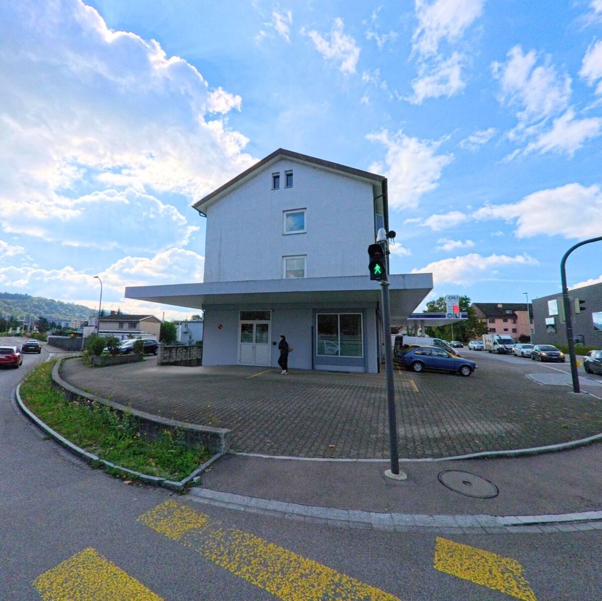 Ein modernes Eckgebäude mit grossem Vordach steht an einer Kreuzung in Laufenburg (5080, Kanton Aargau), daneben führt eine Strasse Richtung Stadtzentrum.