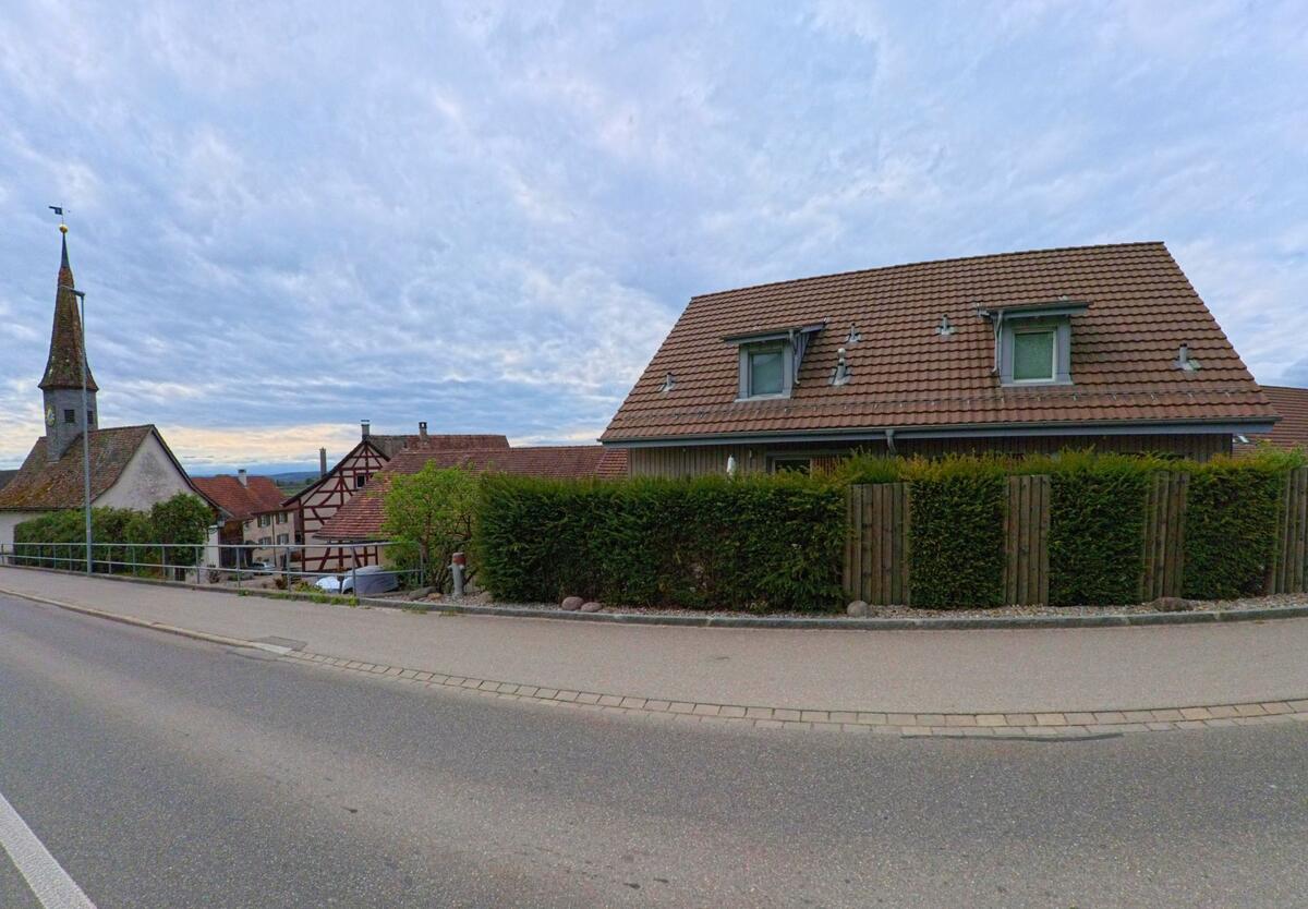 In Laufen-Uhwiesen im Kanton Zürich, PLZ 8248, verläuft eine Strasse mit Blick auf die Dorfkirche und traditionelle Fachwerkhäuser.