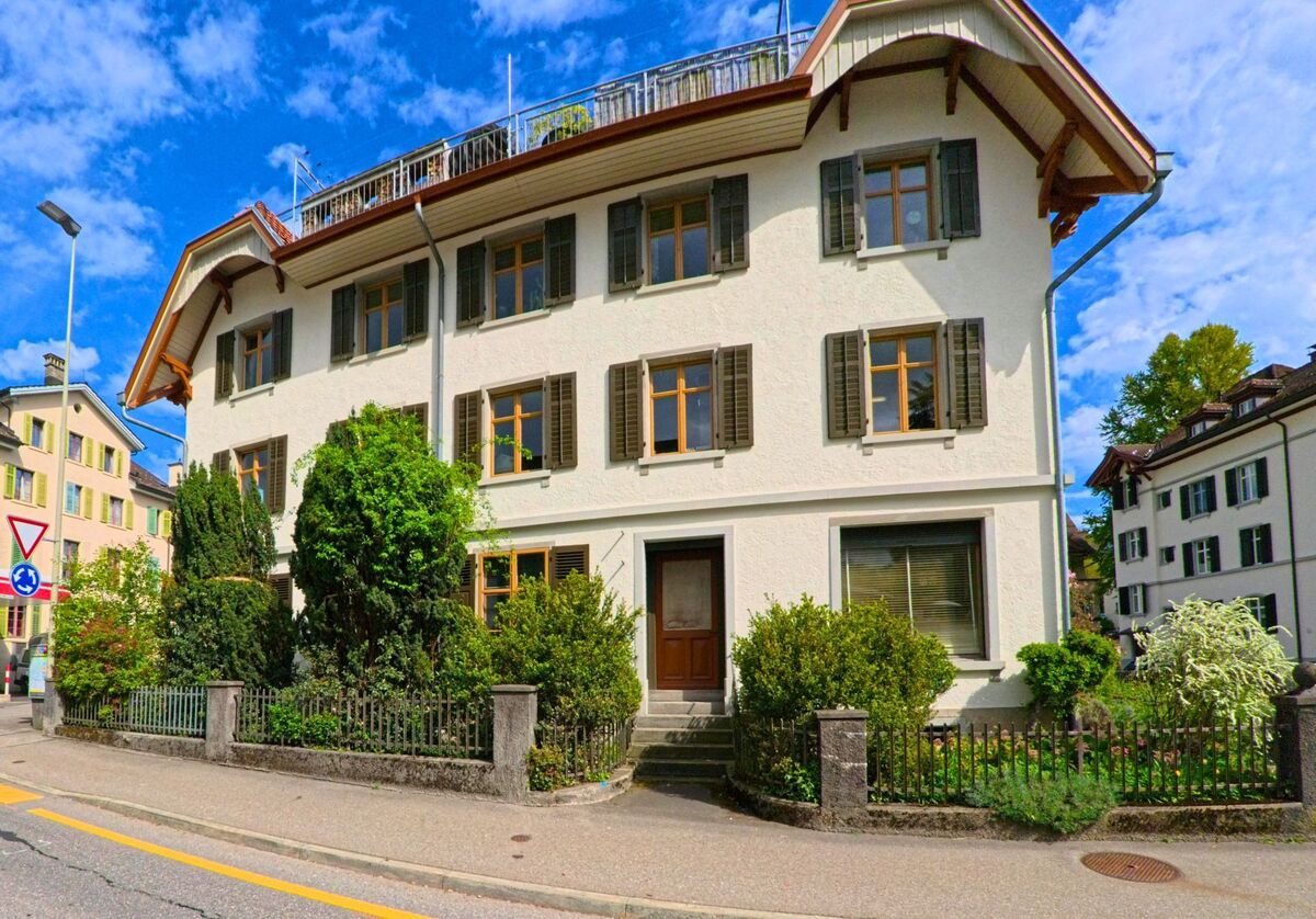 In Laupen (8636, Kanton Bern) steht eine kleine AVIA-Tankstelle neben Wohnhäusern mit gepflegten Vorgärten und grünen Fensterläden an einer Kurve.