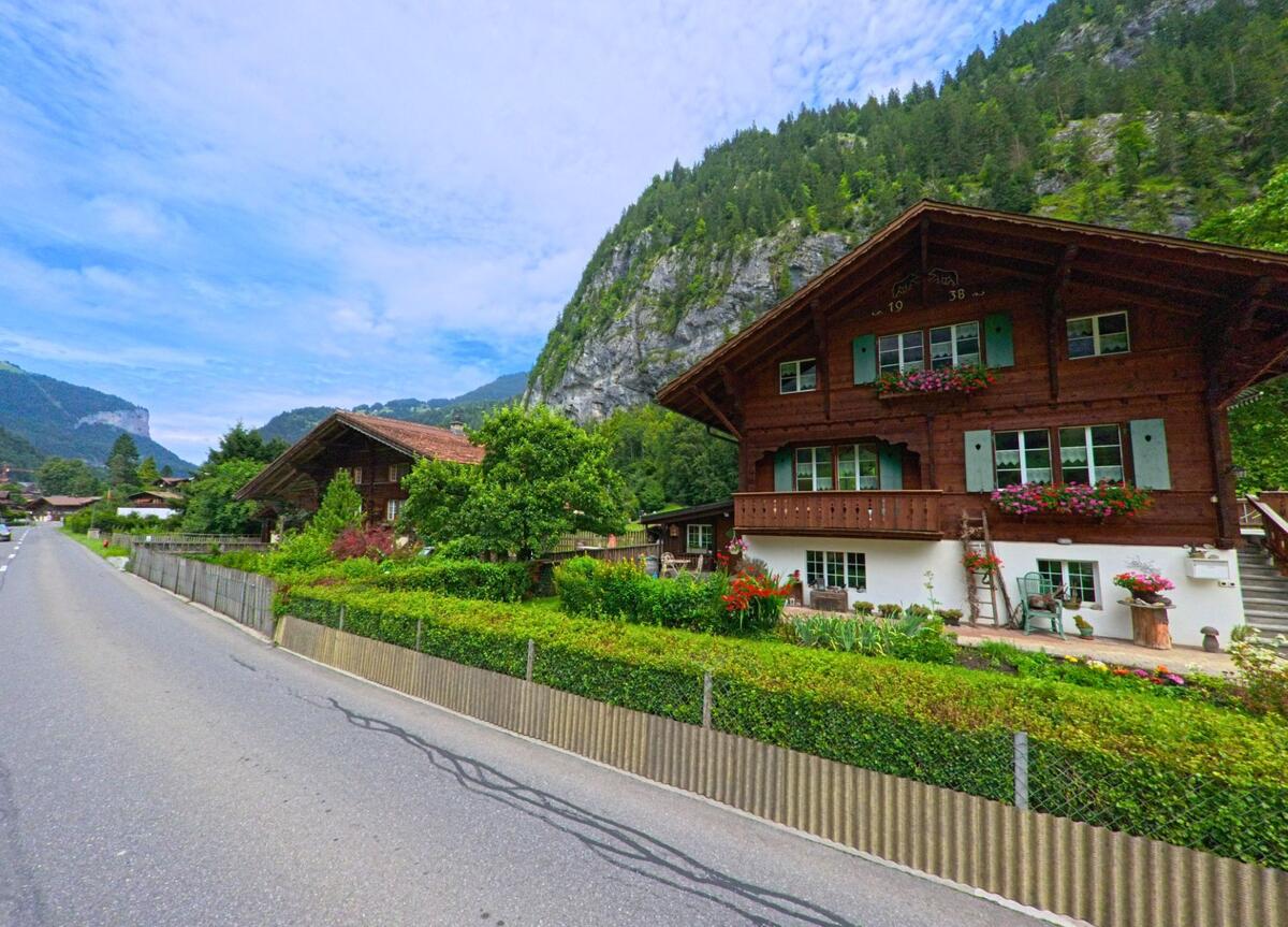Ein gepflegtes Chalet mit Blumenschmuck und Garten liegt in Lauterbrunnen (3822, Kanton Bern) am Strassenrand, im Hintergrund erhebt sich eine bewaldete Felskulisse.