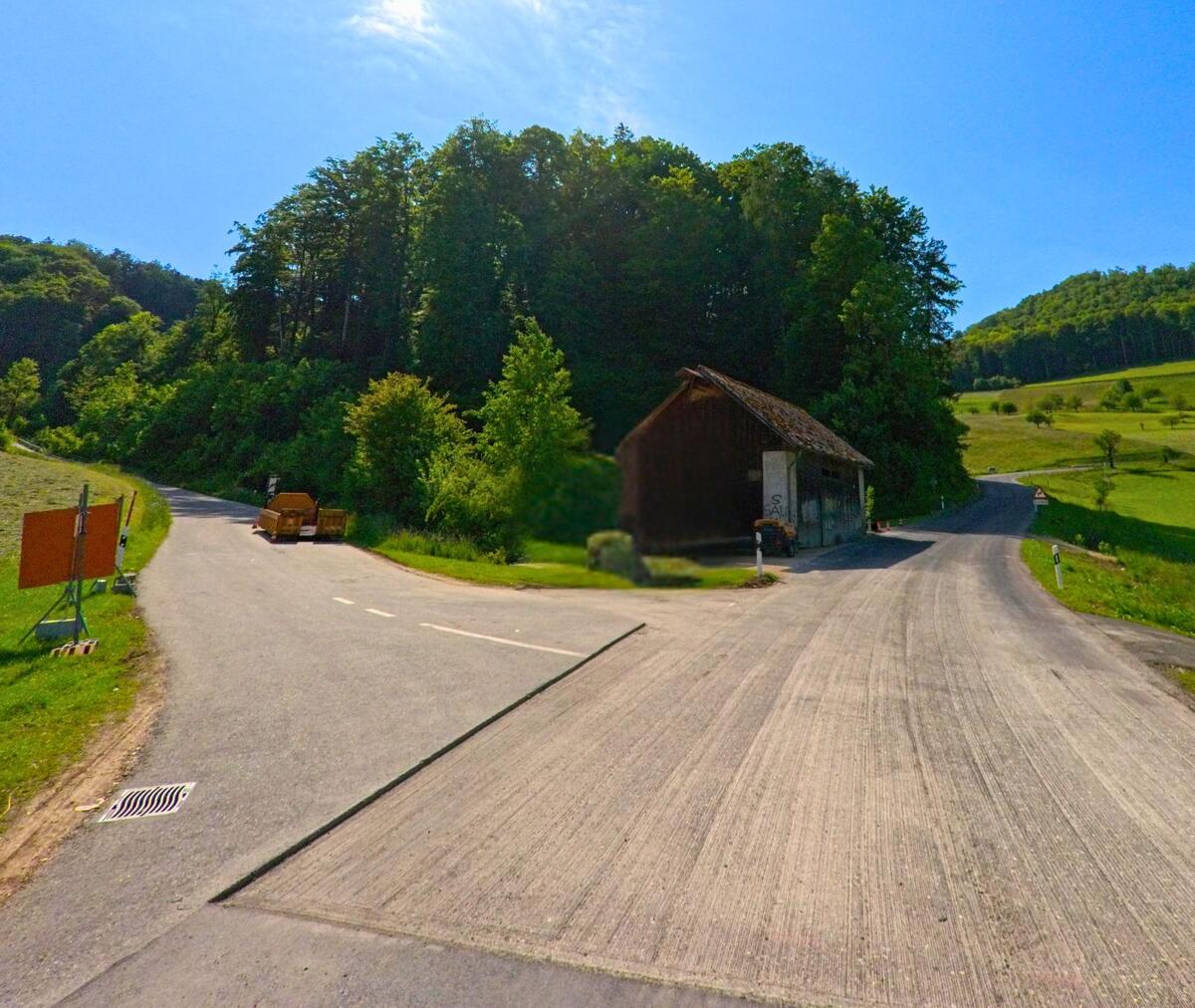 In Lauwil (4426, Kanton Baselland) führt eine Strasse in den Wald, vorbei an einem Bauernhof und weitläufigen Wiesen, während die Sonne den Himmel erleuchtet.
