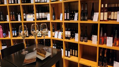 Im Lavaux Vinorama in Rivaz (1071, Kanton Waadt) stehen zahlreiche Weinflaschen in Holzregalen, vor denen ein Tisch mit Weinglaesern und einer kleinen Degustation gedeckt ist.