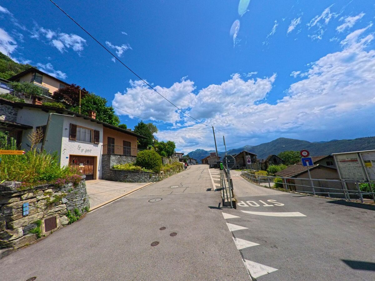 Eine ruhige Strasse mit traditionellen Steinhaeusern fuehrt durch das Dorfzentrum von Lavertezzo (6595, Kanton Tessin) mit Blick auf die umliegenden Berge.