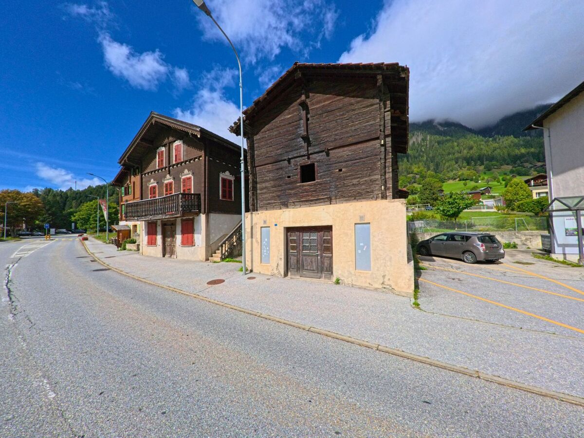 An der Hauptstrasse von Lax (3994, Kanton Wallis) stehen traditionelle Holzhäuser mit roten Fensterlaeden und Balkonen vor der Kulisse gruener Berghaenge.