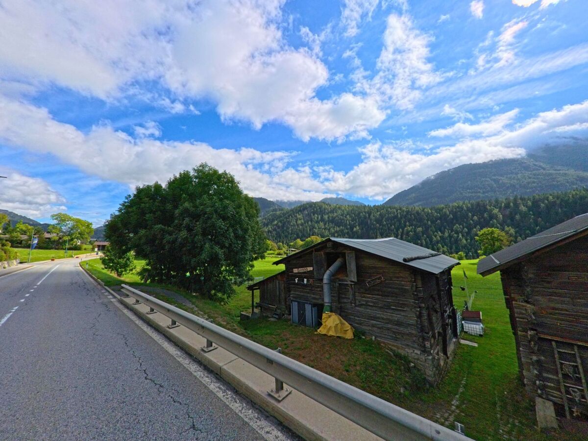 Am Ortsrand von Lax (3994, Kanton Wallis) stehen alte Speicherhaeuser aus Holz auf einer Wiese, umgeben von Bergen und Wäldern.