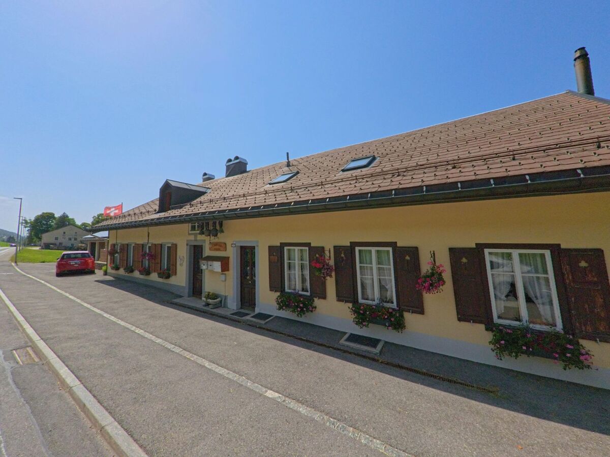 In Le Chenit (1348, Kanton Waadt) untersucht ein Kammerjaeger ein langgezogenes Wohnhaus mit Blumenkaesten und braunen Fensterlaeden.