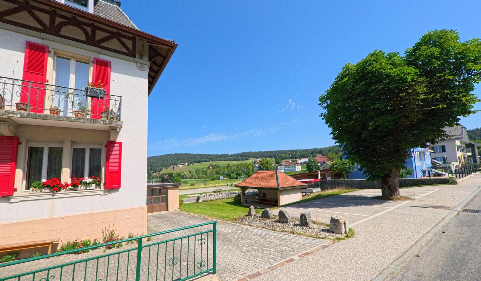 In Le Lieu (1343, Kanton Waadt) inspiziert ein Kammerjaeger ein Wohnhaus mit roten Fensterlaeden und Blick auf die umliegende Landschaft.
