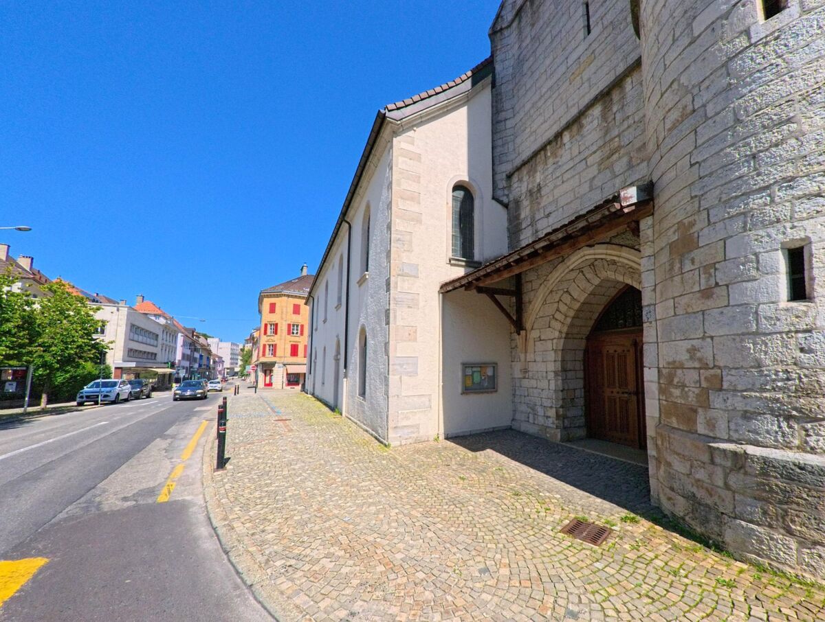 Eine gepflasterte Strasse in Le Locle (2400, Kanton Neuenburg) fuehrt an einem historischen Gebaeude mit rundem Turm und Holztor vorbei.