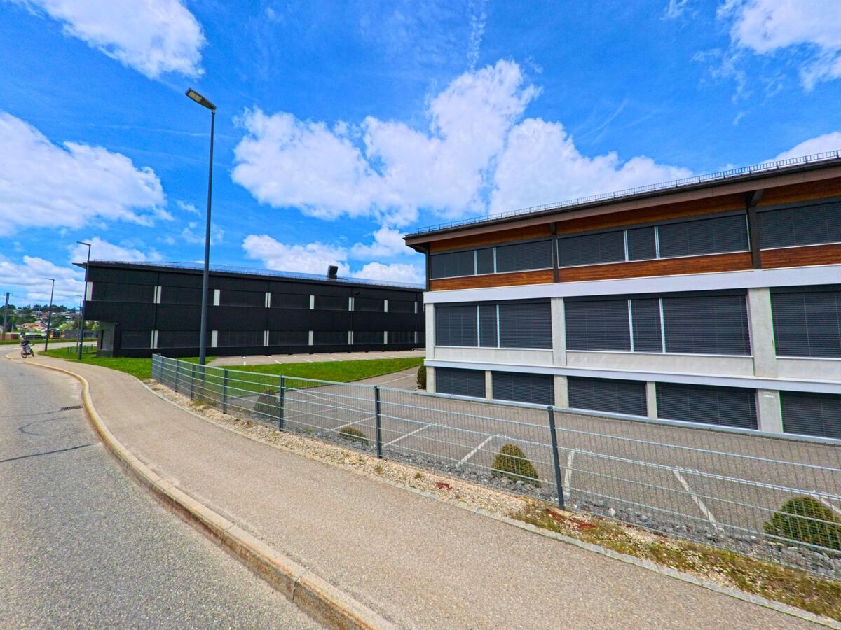 In Le Noirmont (2340, Kanton Jura) sind moderne, zweigeschossige Gebäude zu sehen, die entlang einer Straße stehen, umgeben von einem Zaun und einem klaren Himmel.