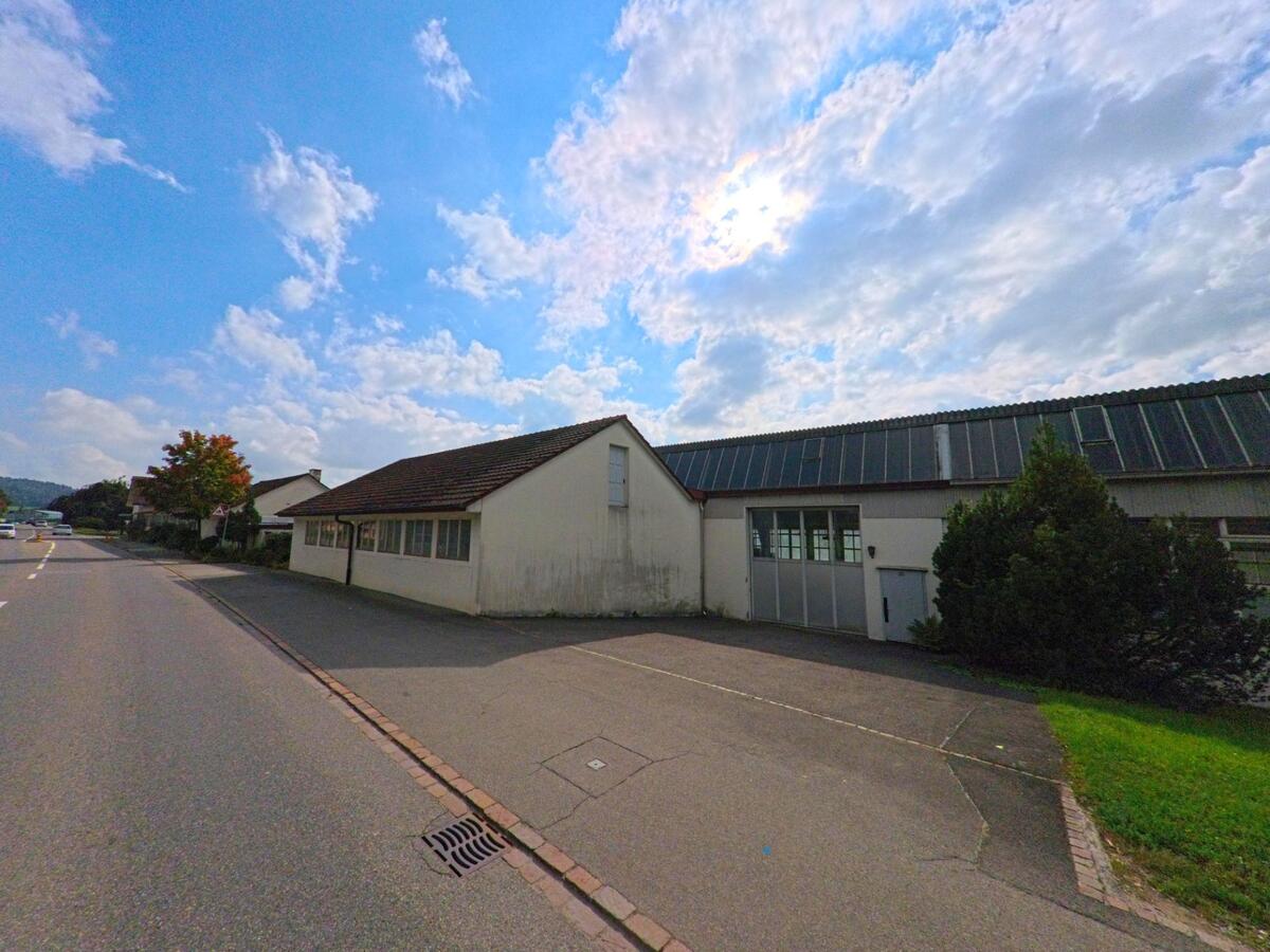 An der Hauptstrasse in Leimbach (5733, Kanton Aargau) stehen mehrere Gewerbegebäude mit Satteldächern, die von der Sonne und leichtem Schatten beleuchtet werden.