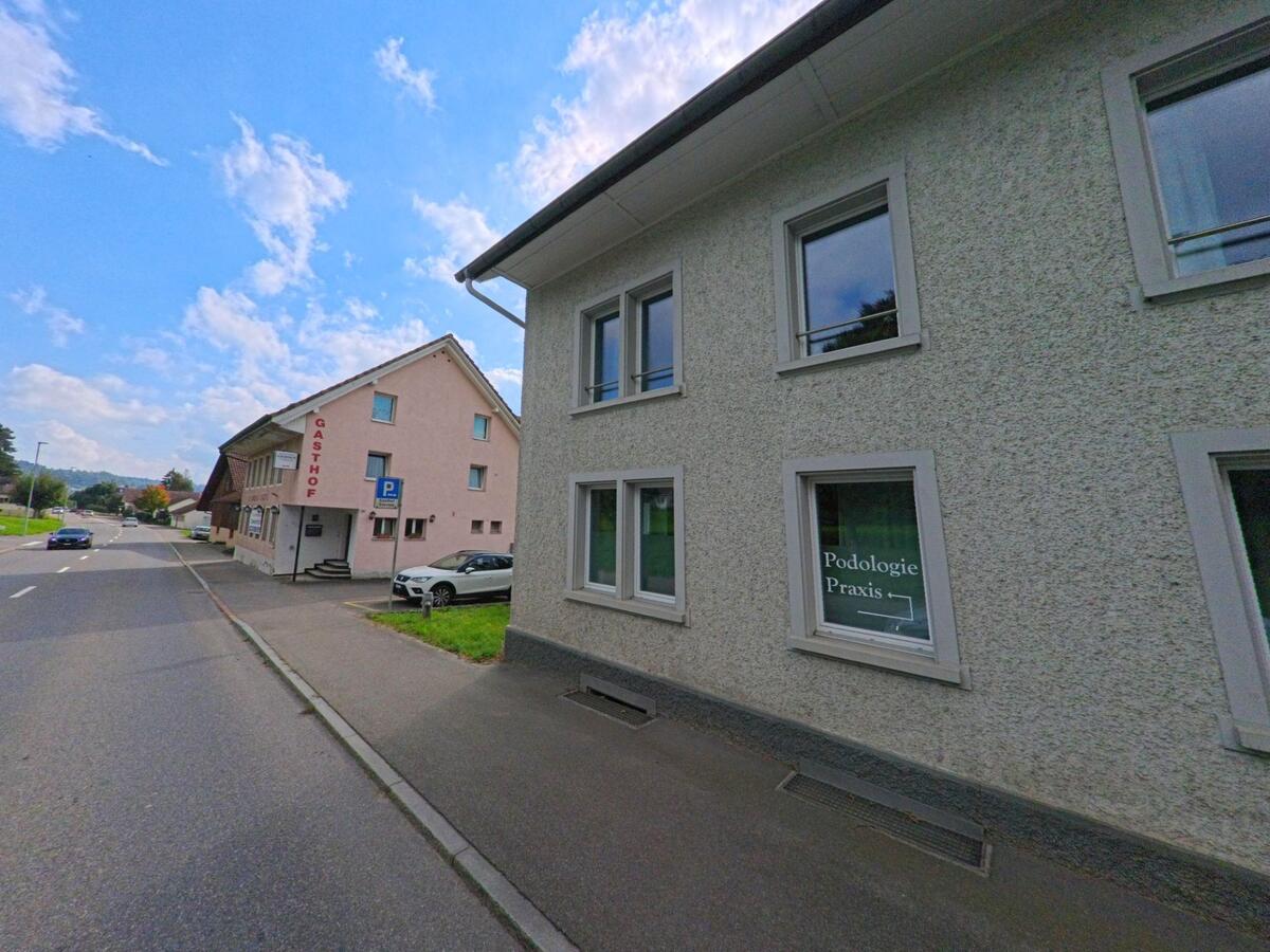 An der Hauptstrasse in Leimbach (5733, Kanton Aargau) liegen eine Podologiepraxis und ein Gasthof, die von vorbeifahrenden Autos passiert werden.