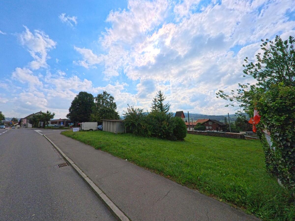 Eine ruhige Quartierstrasse in Leimbach (5733, Kanton Aargau) führt an gepflegten Gärten und Einfamilienhäusern vorbei, im Hintergrund öffnet sich der Blick auf das Tal.
