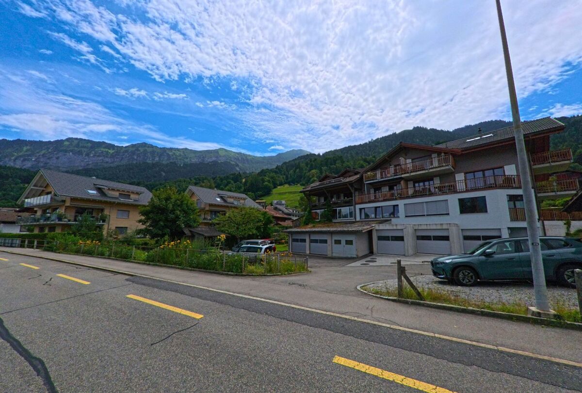 Mehrfamilienhaeuser mit Balkonen stehen in Leissigen (3706, Kanton Bern) am Fusse eines bewaldeten Berghangs mit Blick auf die umliegende Landschaft.
