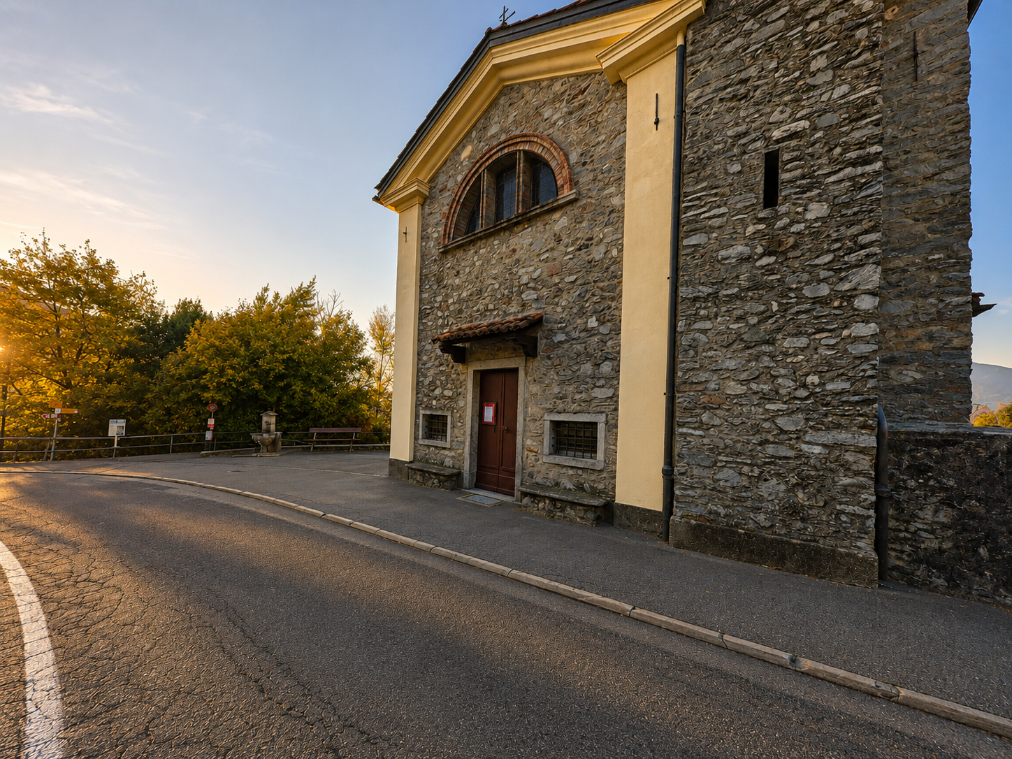 An einer ruhigen Strasse in Lema (6981, Kanton Tessin) steht eine Kirche mit Natursteinfassade, Rundbogenfenster und schlichtem Eingangsportal.