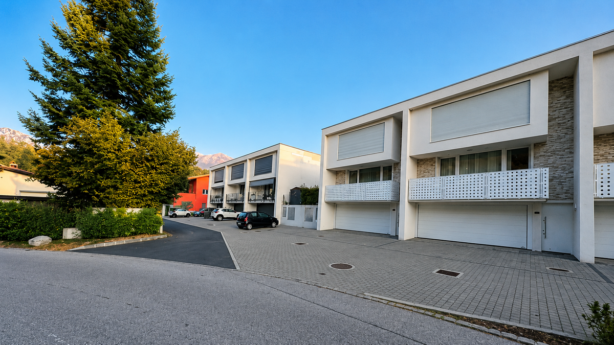 : Moderne Wohnhäuser mit grossen Garagentoren und hellen Balkonen säumen eine ruhige Strasse in Lema (6986, Kanton Tessin).
