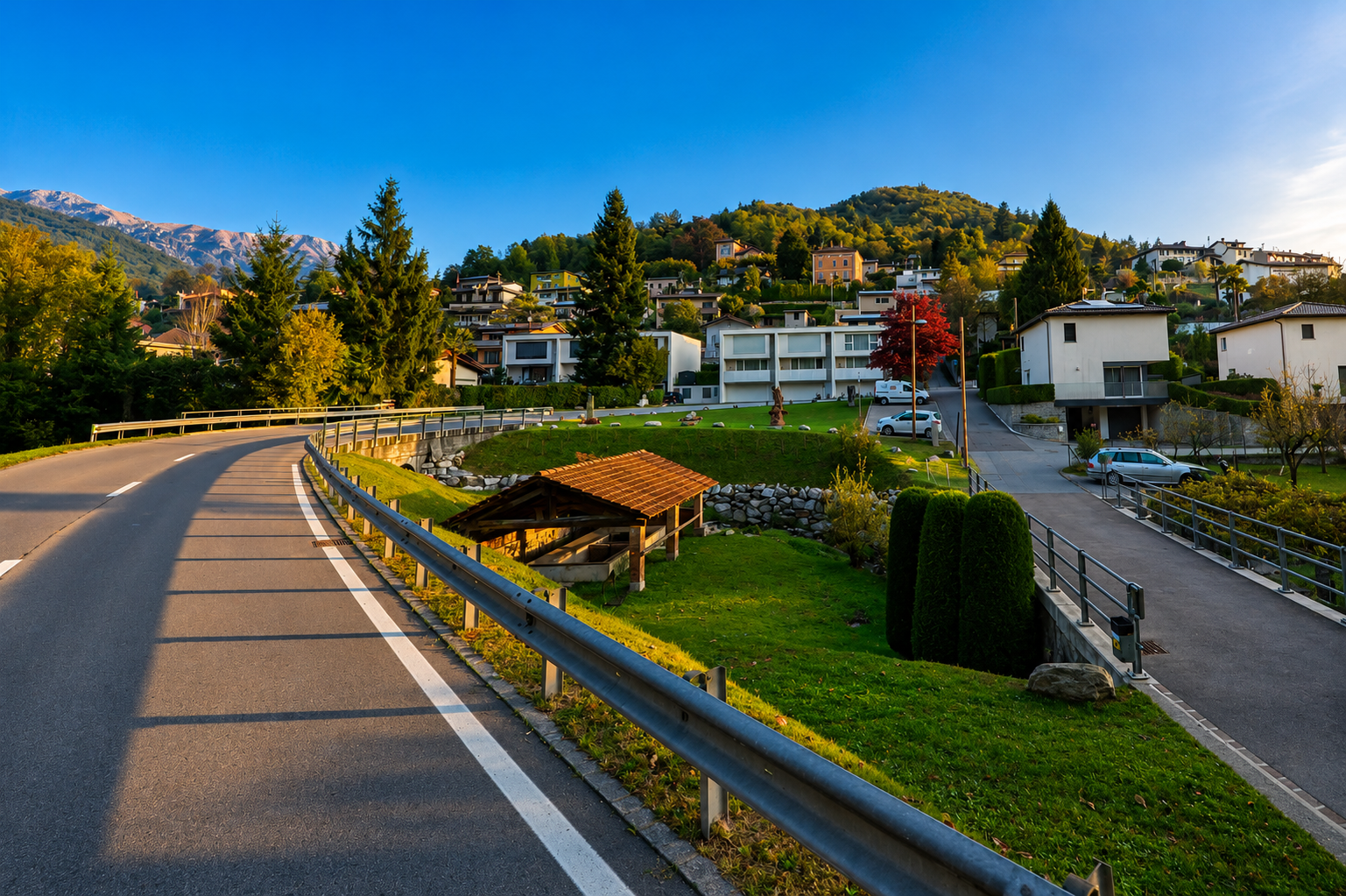 Entlang einer kurvigen Strasse in Lema (6986, Kanton Tessin) stehen moderne Wohnhäuser zwischen Grünflächen und bewaldeten Hängen.