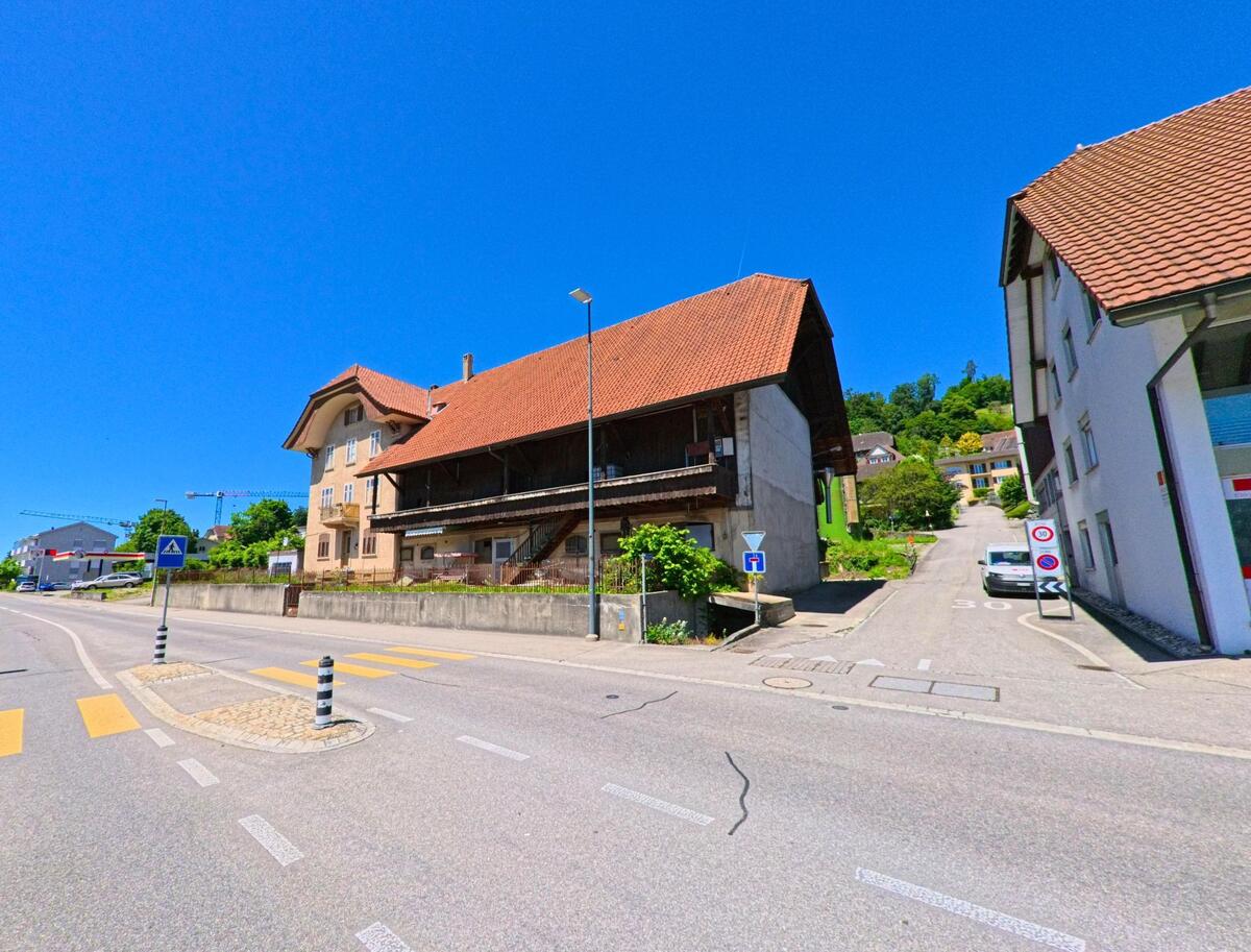 In Lengnau (2543, Kanton Bern) führt eine breite Straße mit einem traditionellen Gebäude und einem steilen Abzweig in den Hügel.