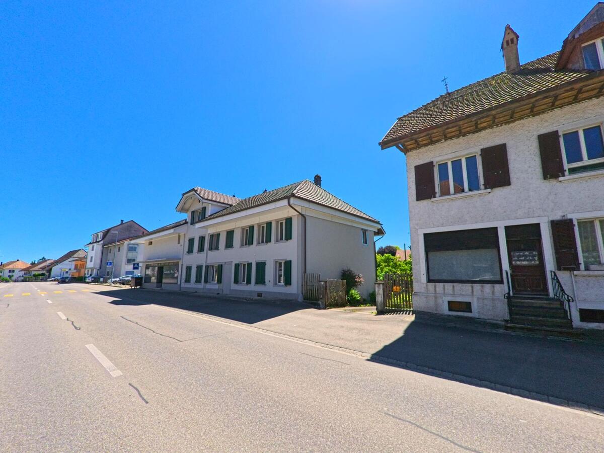 In Lengnau (2543, Kanton Bern) verläuft eine sonnige Straße mit traditionellen Häusern und einem modernen Gebäude auf der linken Seite.