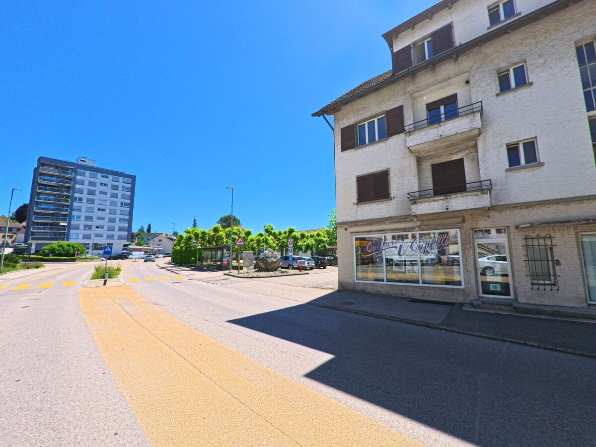 In Lengnau (2543, Kanton Bern) verläuft eine breite Straße mit einem modernen Gebäude auf der linken Seite und einem historischen Gebäude auf der rechten Seite.