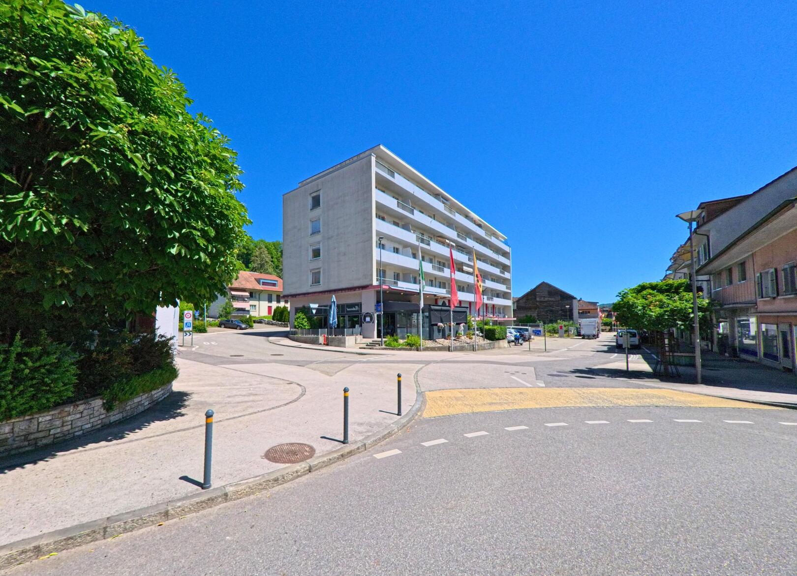 In Lengnau (2543, Kanton Bern) zeigt das Bild eine belebte Strassenecke mit einem modernen Gebäude und einem grünen Baum auf der rechten Seite.