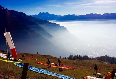 Auf einem Hang oberhalb von Noville (1845, Kanton Waadt) bereiten Gleitschirmflieger ihre Schirme bei klarem Wetter mit Nebel im Tal für den Start vor.Auf einem Hang oberhalb von Noville (1845, Kanton Waadt) bereiten Gleitschirmflieger ihre Schirme bei klarem Wetter mit Nebel im Tal für den Start vor.