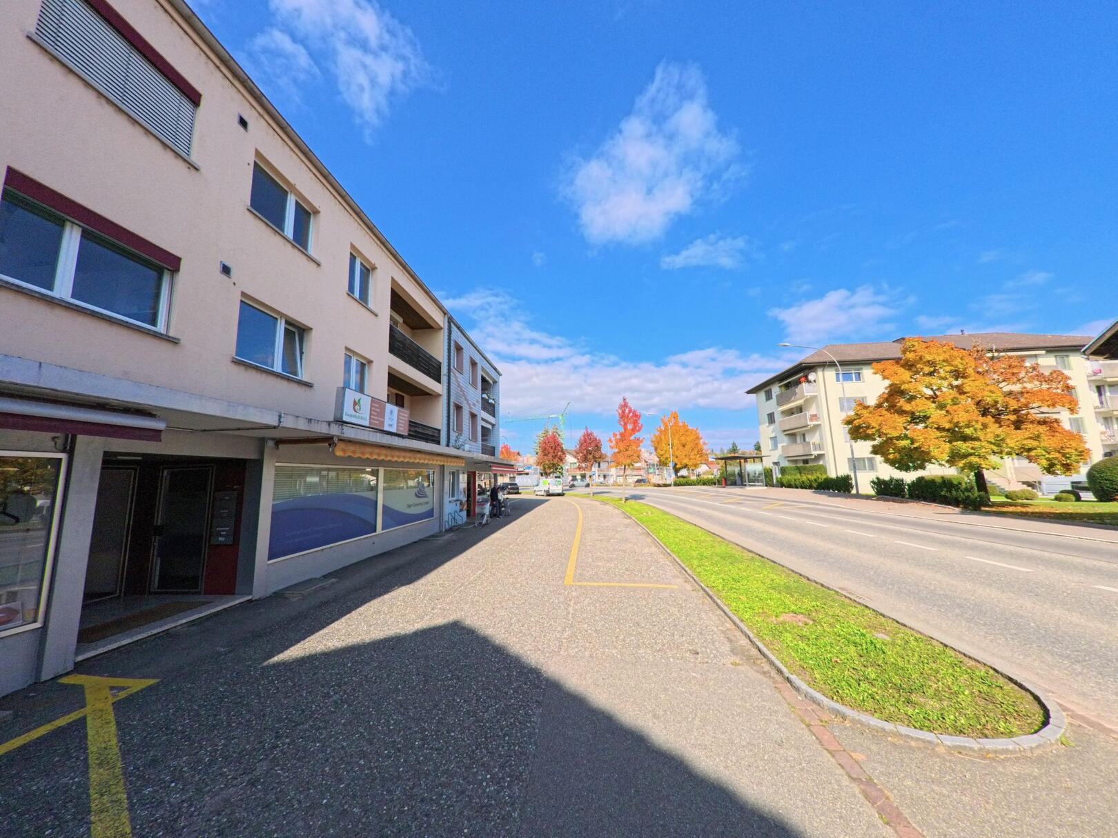 Entlang der Hauptstrasse in Leuggern (5316, Kanton Aargau) reihen sich Wohn- und Geschäftshäuser unter einem klaren Herbsthimmel aneinander.