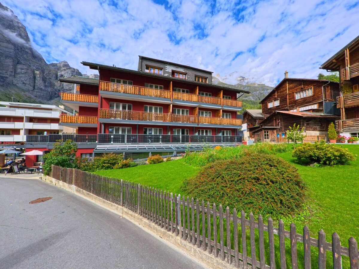 Eine bepflanzte Verkehrsinsel mit bunten Blumen schmueckt eine Strassenkreuzung in Leukerbad (3954, Kanton Wallis), waehrend dahinter Chalets und Hotels am Hang liegen.
