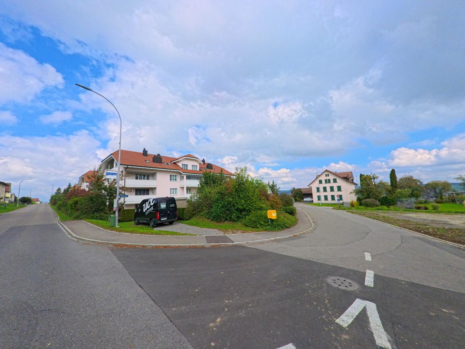 Am Dorfrand von Leutwil (5725, Kanton Aargau) treffen zwei Strassen aufeinander, gesäumt von modernen Mehrfamilienhäusern und einem älteren Wohnhaus.