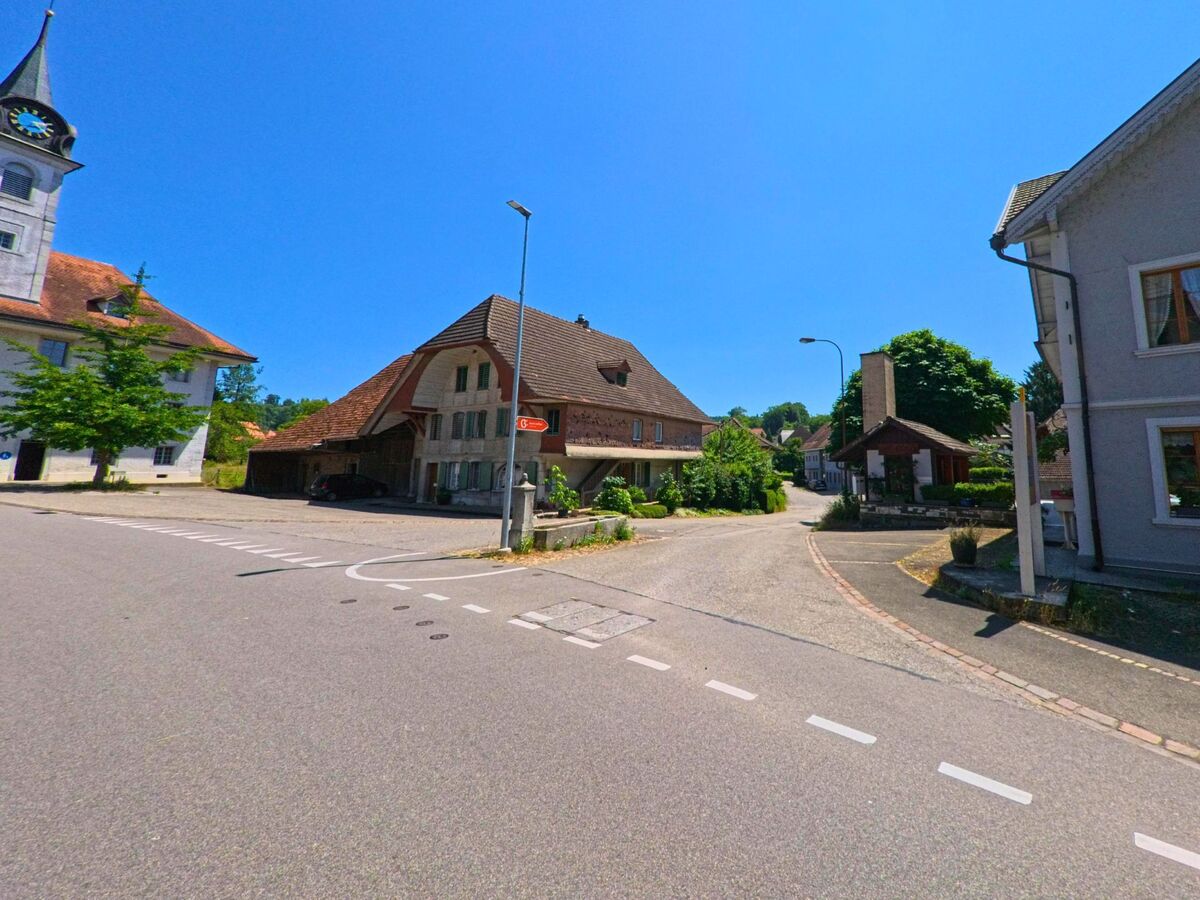 Im Zentrum von Leuzigen (3297, Kanton Bern) treffen sich mehrere Strassen vor der Kirche und einem traditionellen Wohnhaus mit Carport.