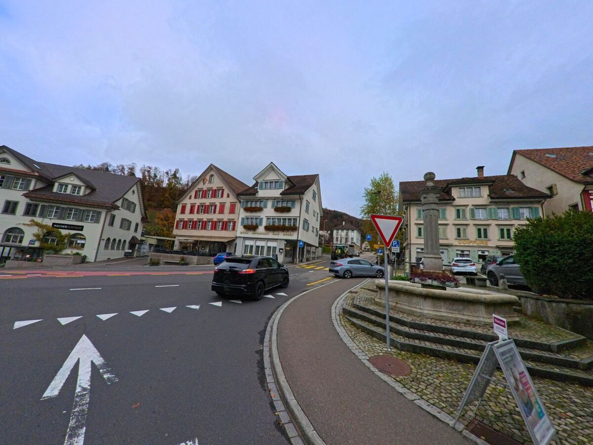 Nahe dem markanten Brunnen vor historischen Haeuserzeilen in Lichtensteig (9620, Kanton St. Gallen) fuehrt eine Hauptstrasse mit klaren Markierungen durch das Ortszentrum.