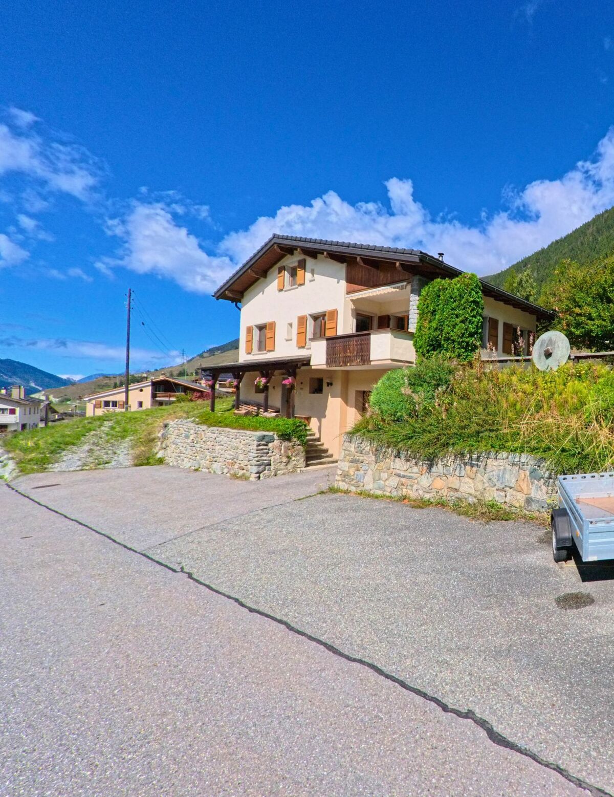 Die Kirche von Liddes (1945, Kanton Wallis) mit ihrem markanten Turm steht auf einer Anhöhe vor bewaldeten Berghaengen und weitem Talblick.