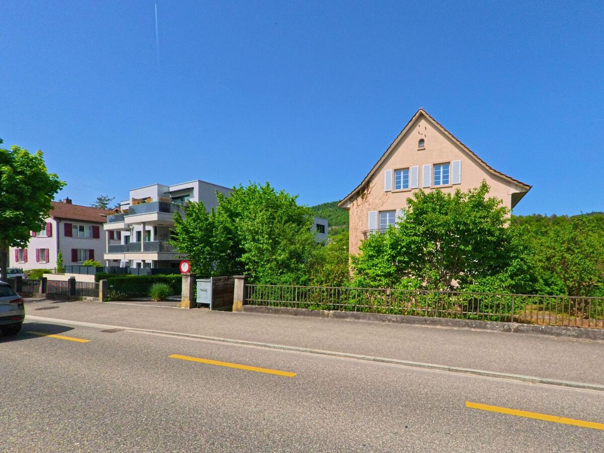 Entlang einer Strasse in Liestal (4410, Kanton Basel-Landschaft) stehen nebeneinander ein älteres Wohnhaus mit hellen Fensterläden und moderne Mehrfamilienhäuser.